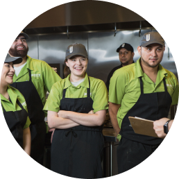 A group of Uberrito Mexican franchise restaurant team members in green aprons are standing in a kitchen.