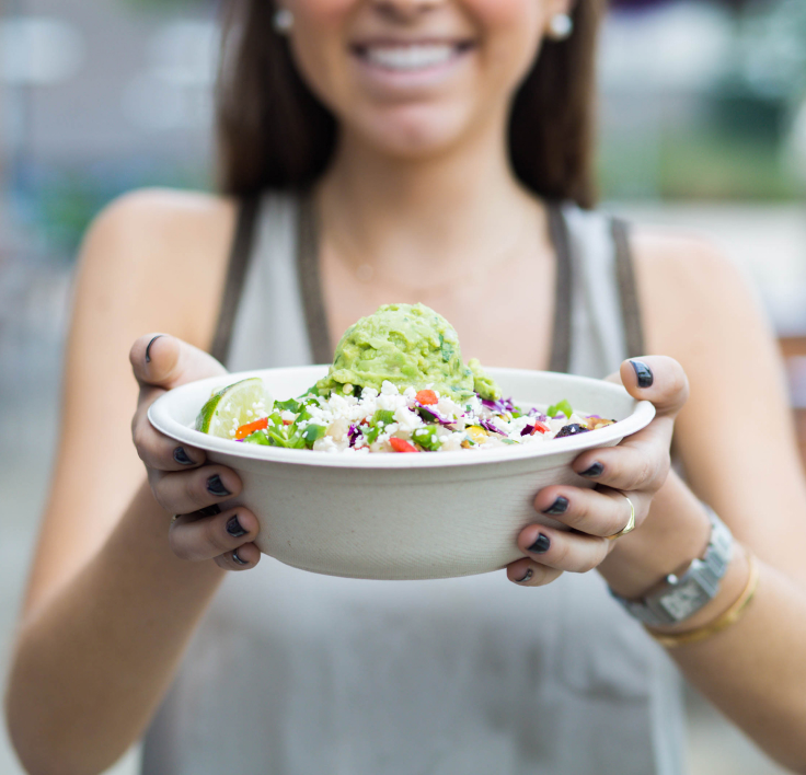 A joyful woman holding a vibrant bowl of a fresh, colorful salad, showcasing a healthy and nutritious meal from Uberrito Mexican franchise
